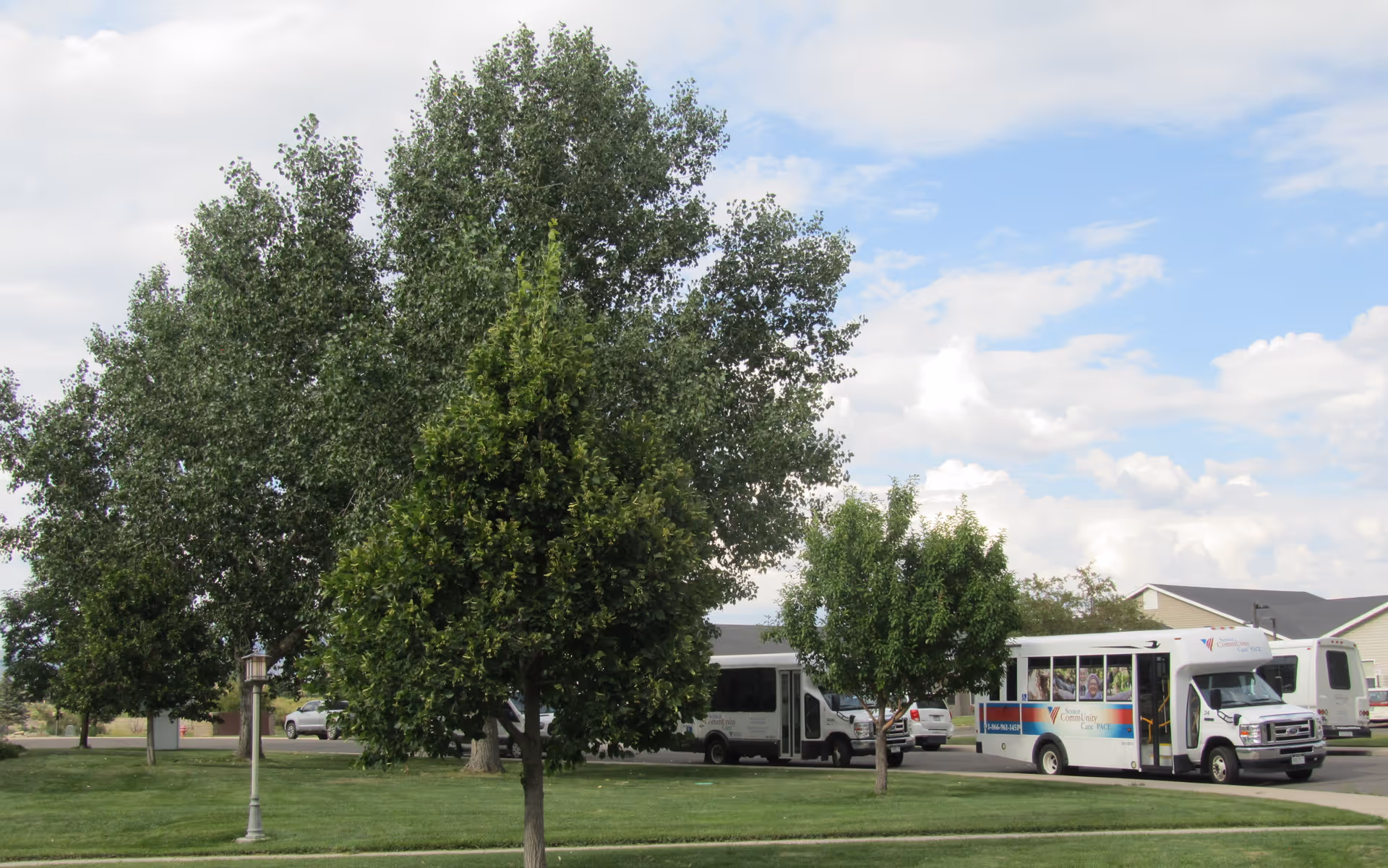 A parking lot with trees and buses in front of a senior care facility.