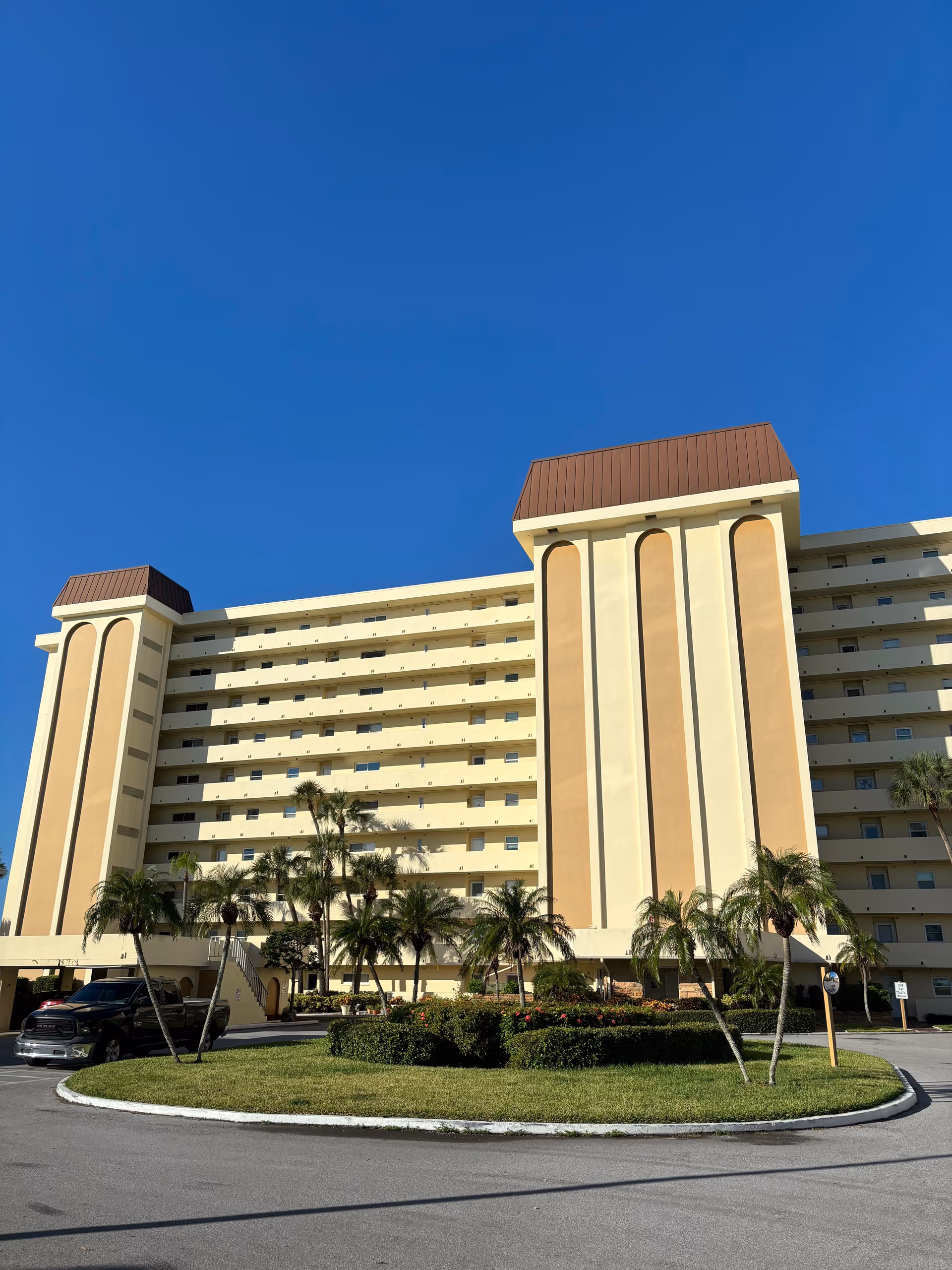 A large beige senior living building with palm trees and a circular driveway.