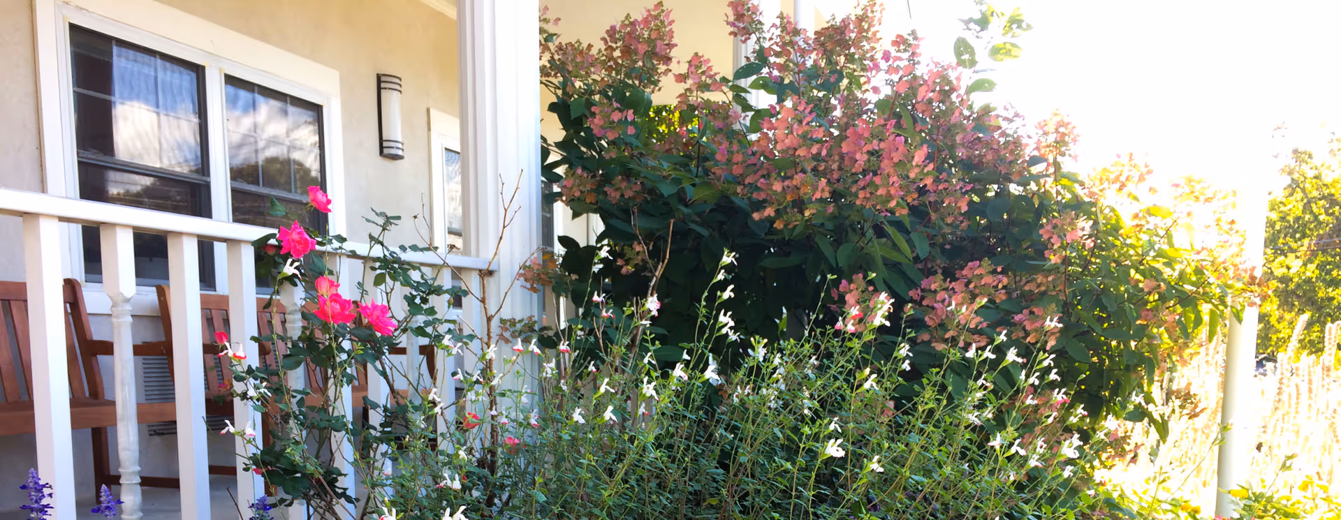 Front porch of a senior living facility with blooming flowers and greenery.