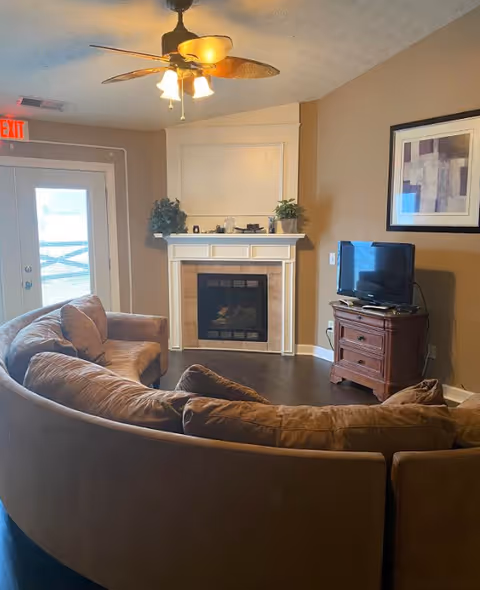 Cozy living room with curved beige sofa, fireplace, mantel decor, and a TV stand.