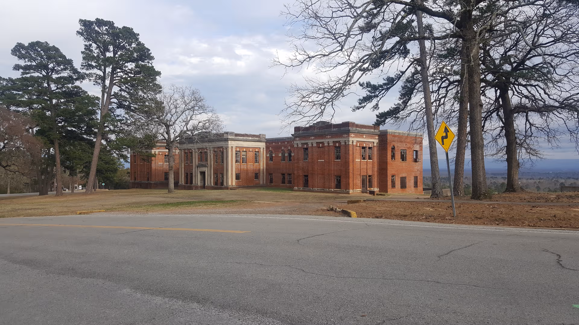 Brick Oklahoma Veterans Center building along a road with tall trees nearby.
