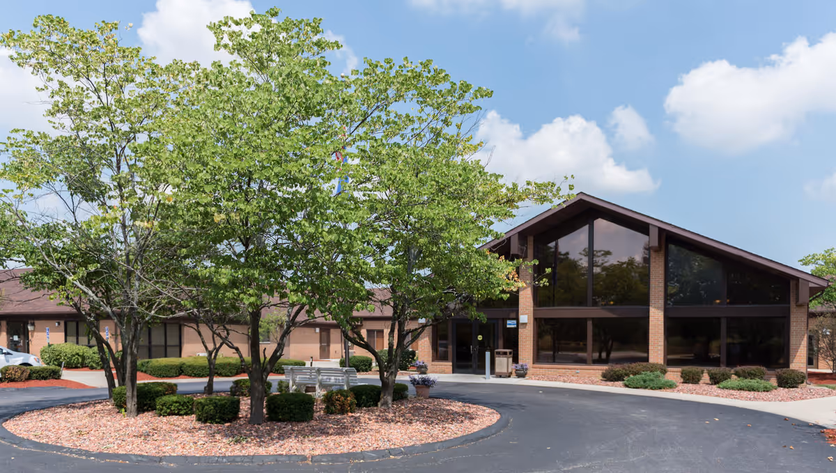 Exterior view of ALIYA of Homewood senior living facility with glass entrance and trees.