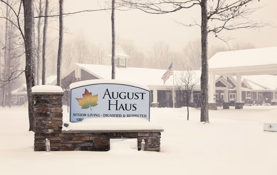 Snow-covered sign for August Haus Assisted Living with the building entrance in background