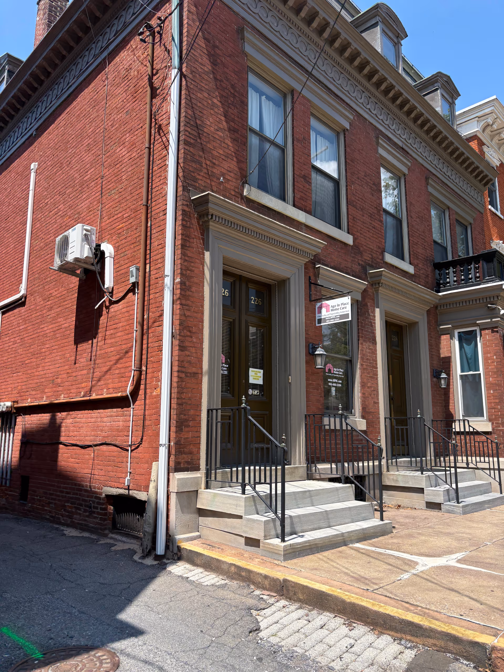 Brick townhouse-style building with two entry doors, stairs, and a visible front sign.