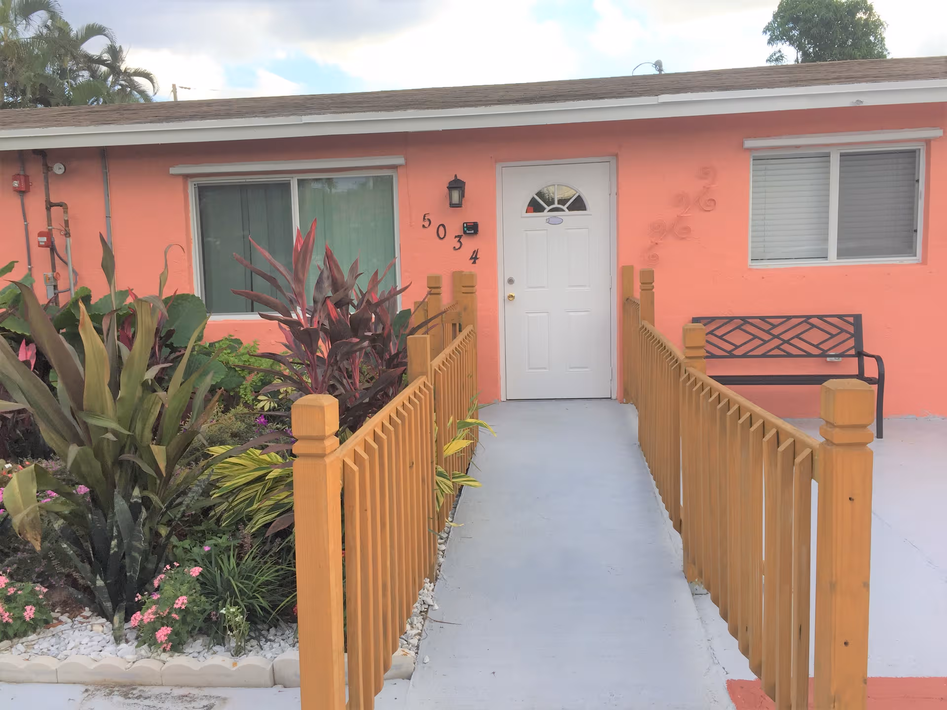 Front entrance of a pink coral building with a walkway, railings, and a bench.