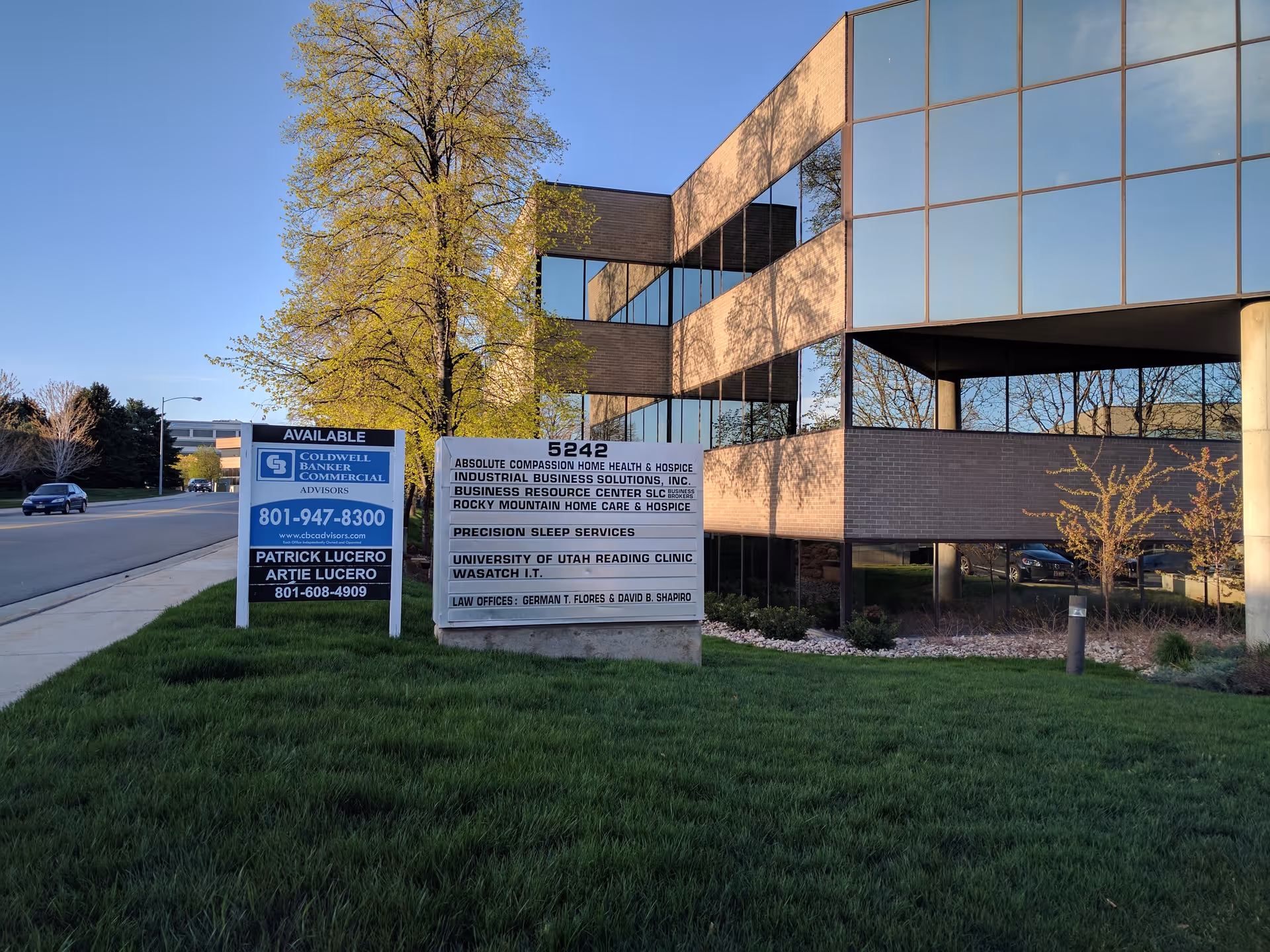 Modern brick building with large glass windows and multiple signboards on a grassy lawn.