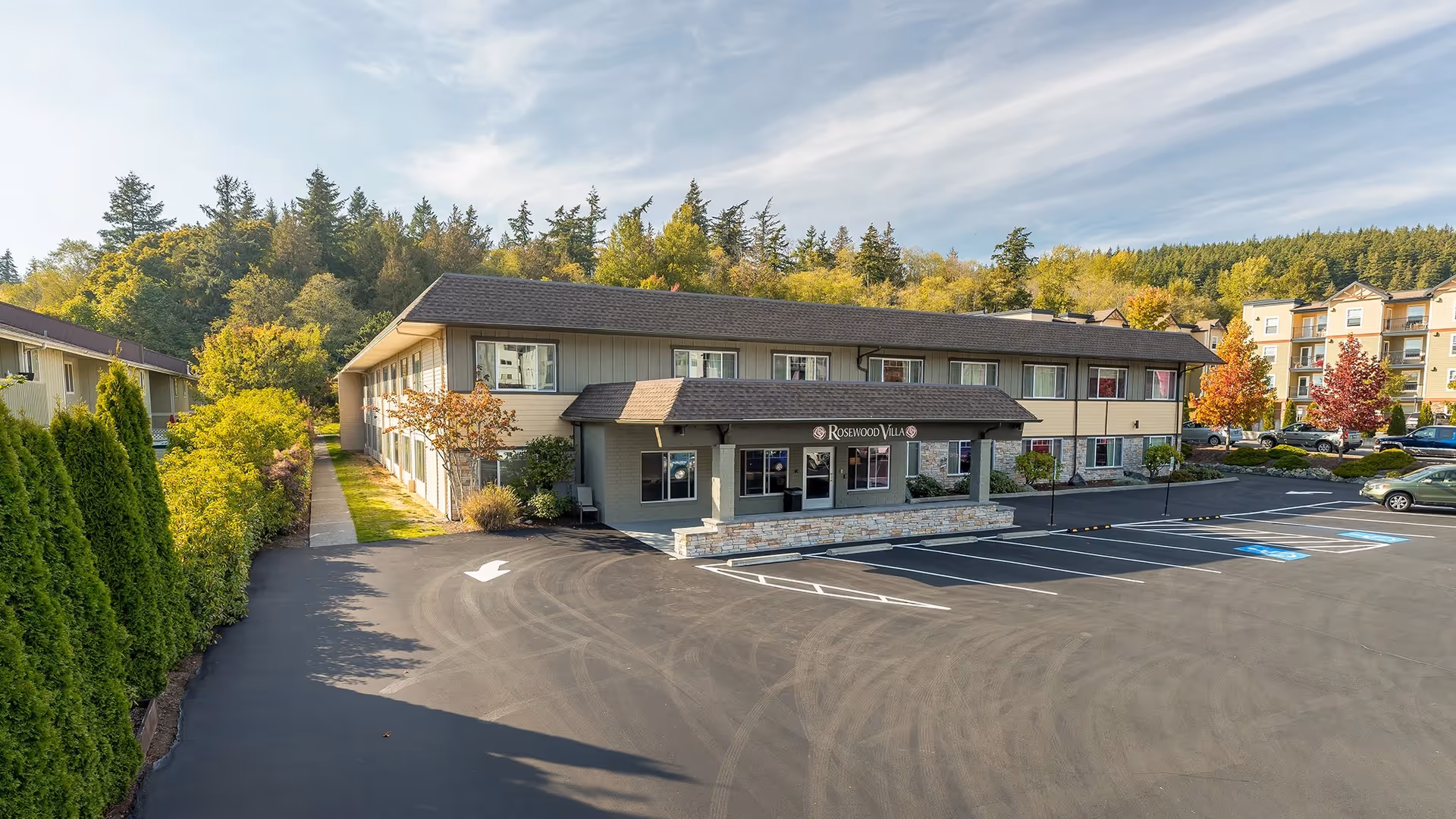 Two-story senior living facility named Rosewood Villa with a parking lot and trees.