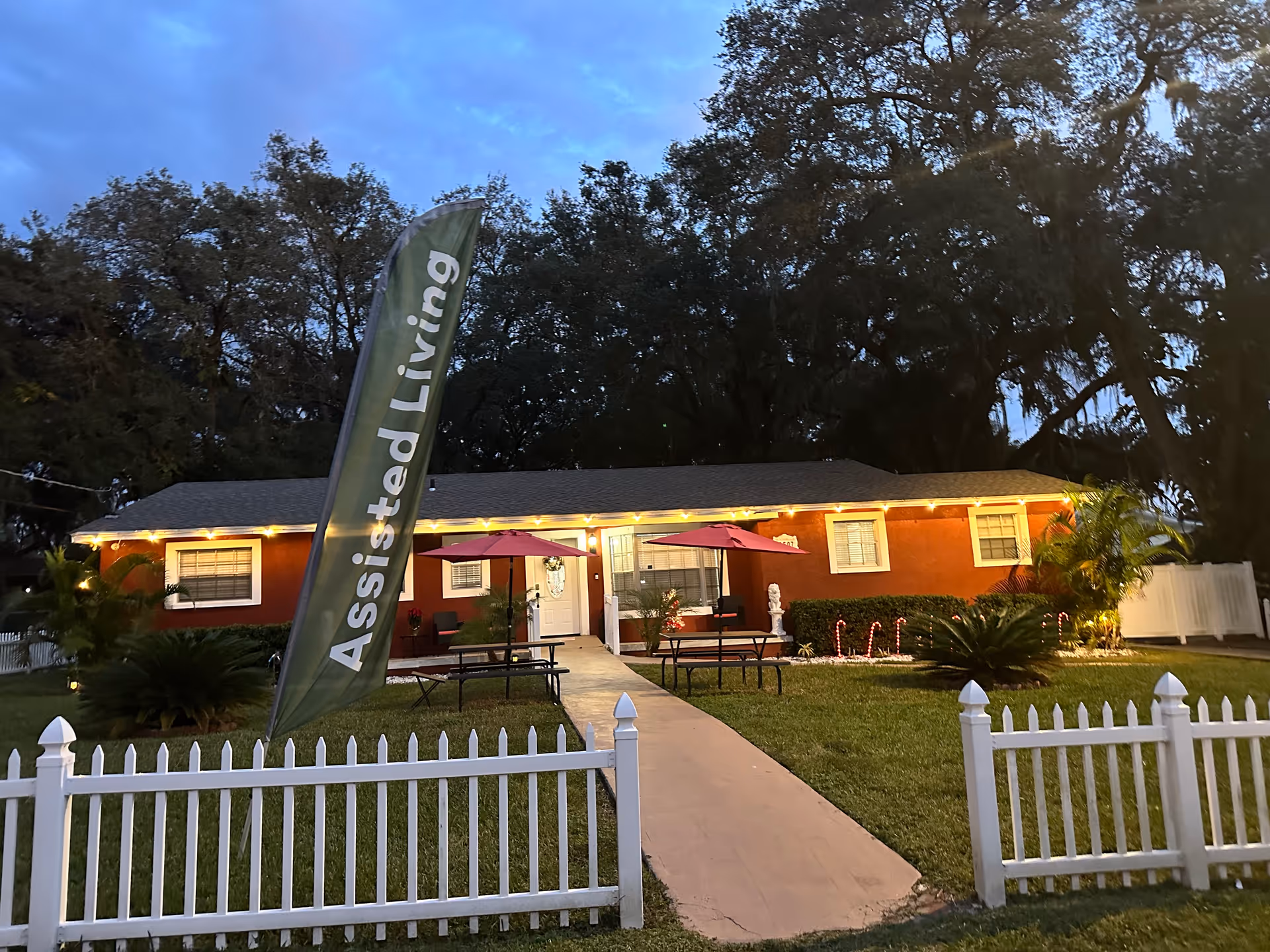 Exterior view of a single-story assisted living facility with flag, fence, and outdoor seating.