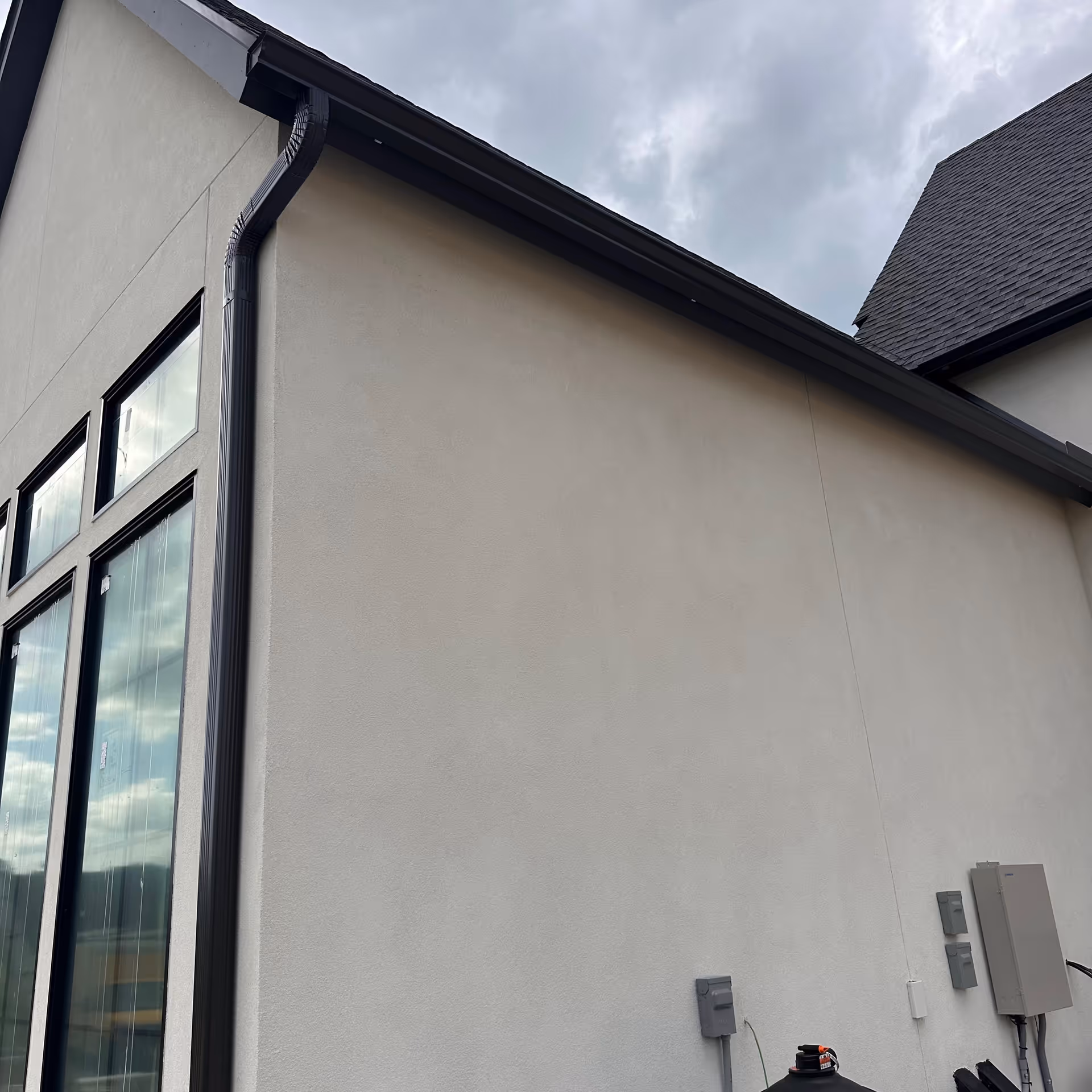 Exterior wall of a modern facility with large glass windows and a downspout.