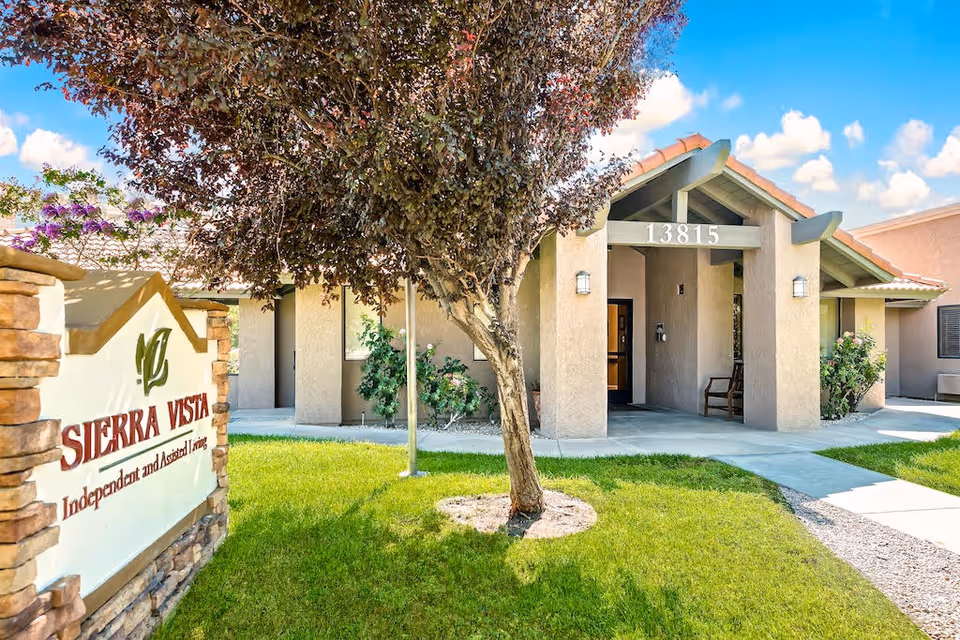 Exterior view of Sierra Vista Independent & Assisted Living entrance with sign, tree, and walkway.