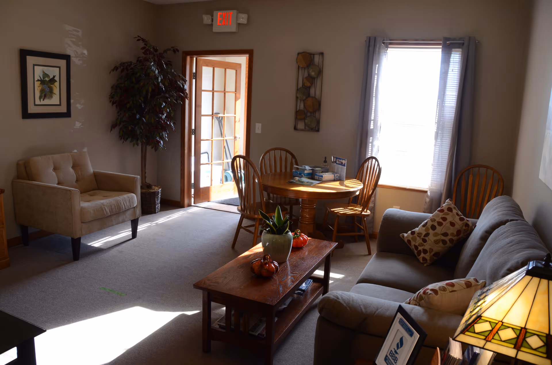 Cozy senior living lounge with sofa, armchair, coffee table, round dining table, and window.