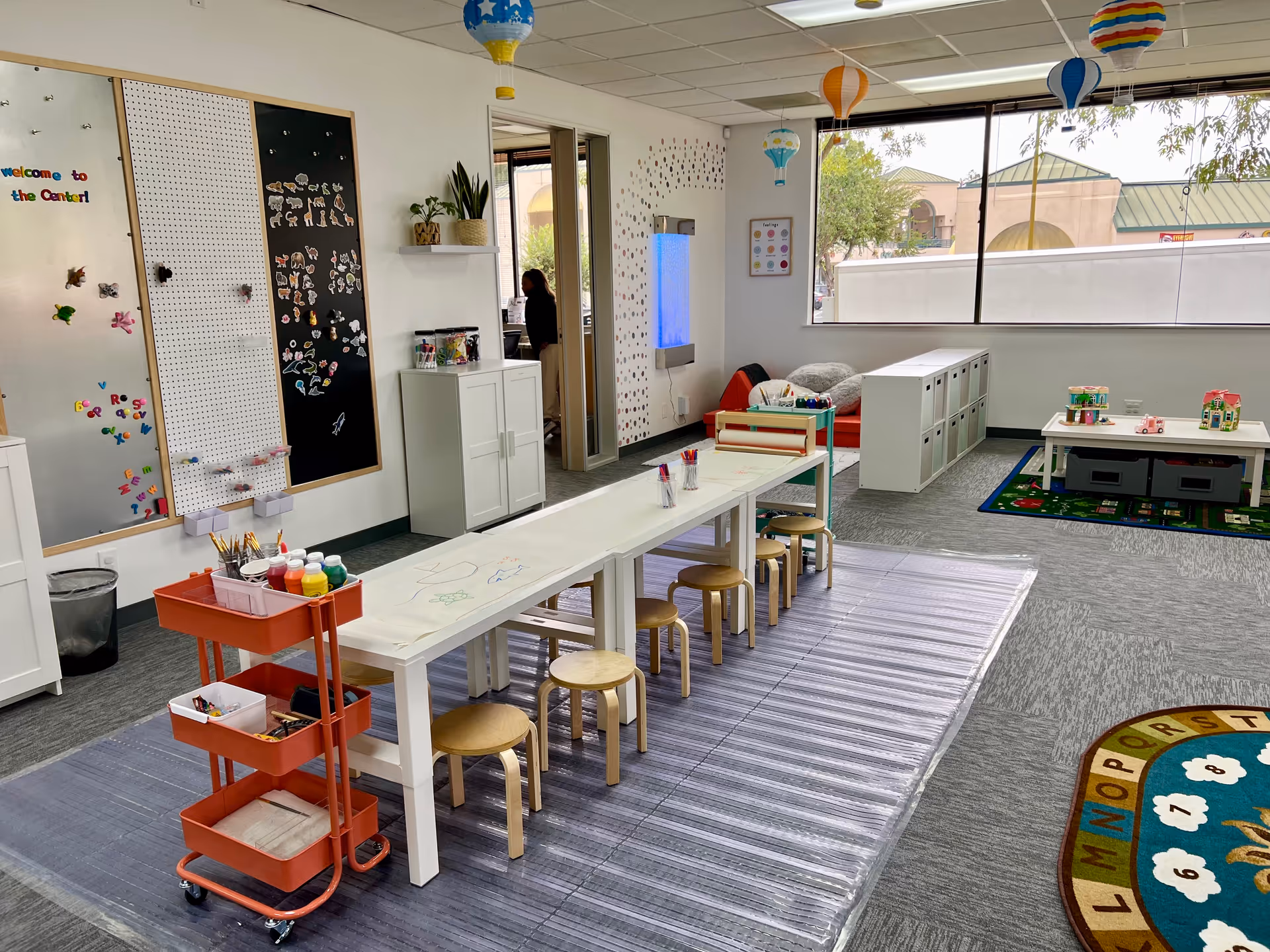 Bright indoor activity room with a long art table, stools, and colorful walls.