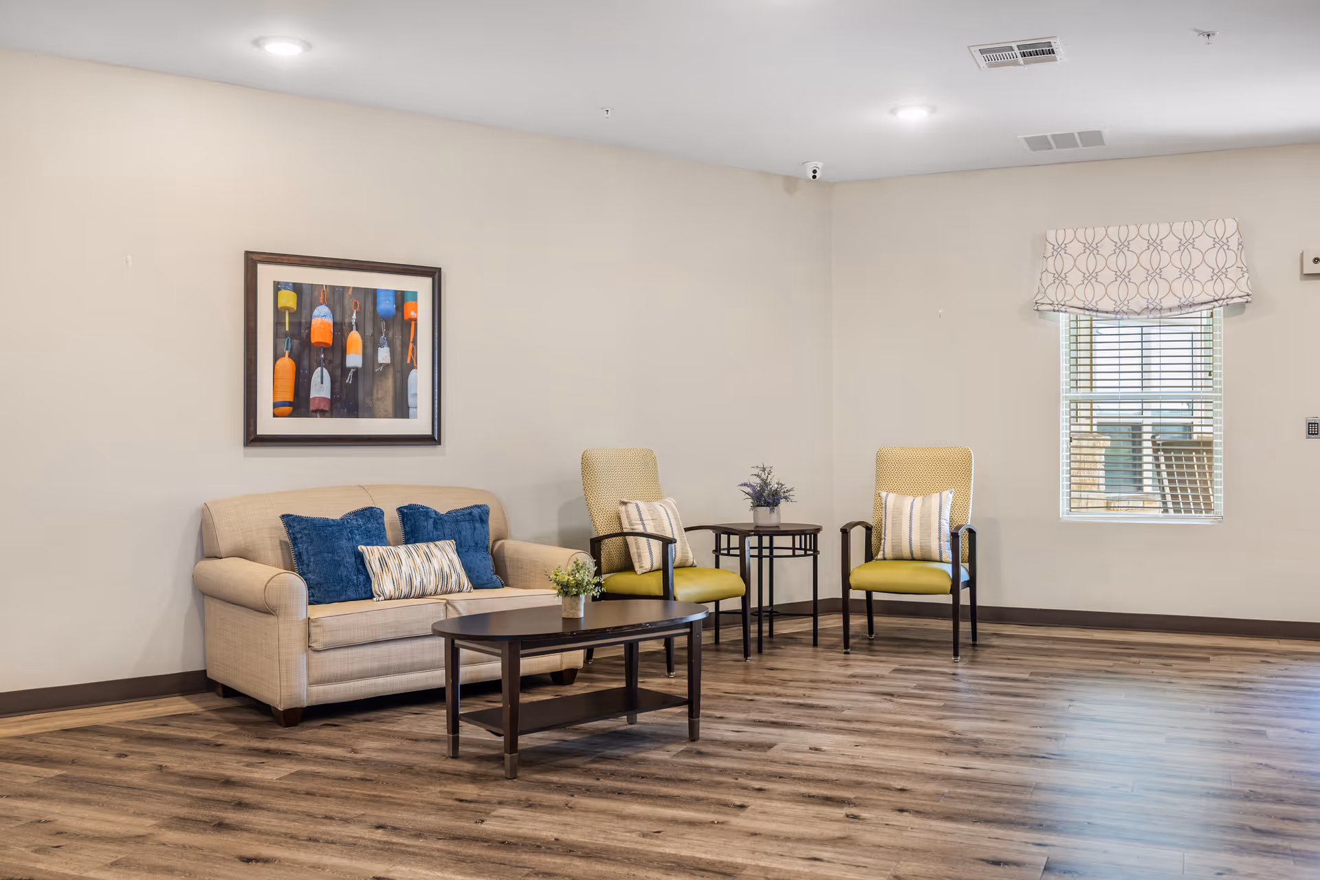 Clean, welcoming lounge with sofa, chairs, tables, art, and a window in neutral tones.