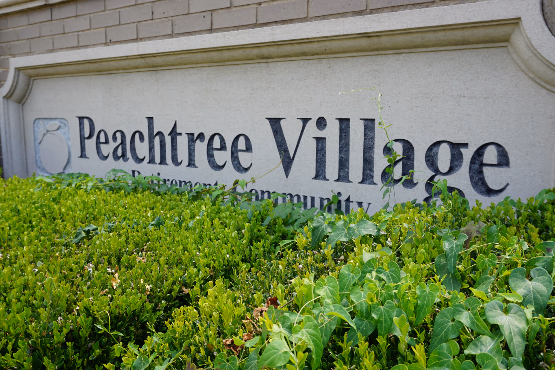 Close-up of Peachtree Village sign with green hedges in front.