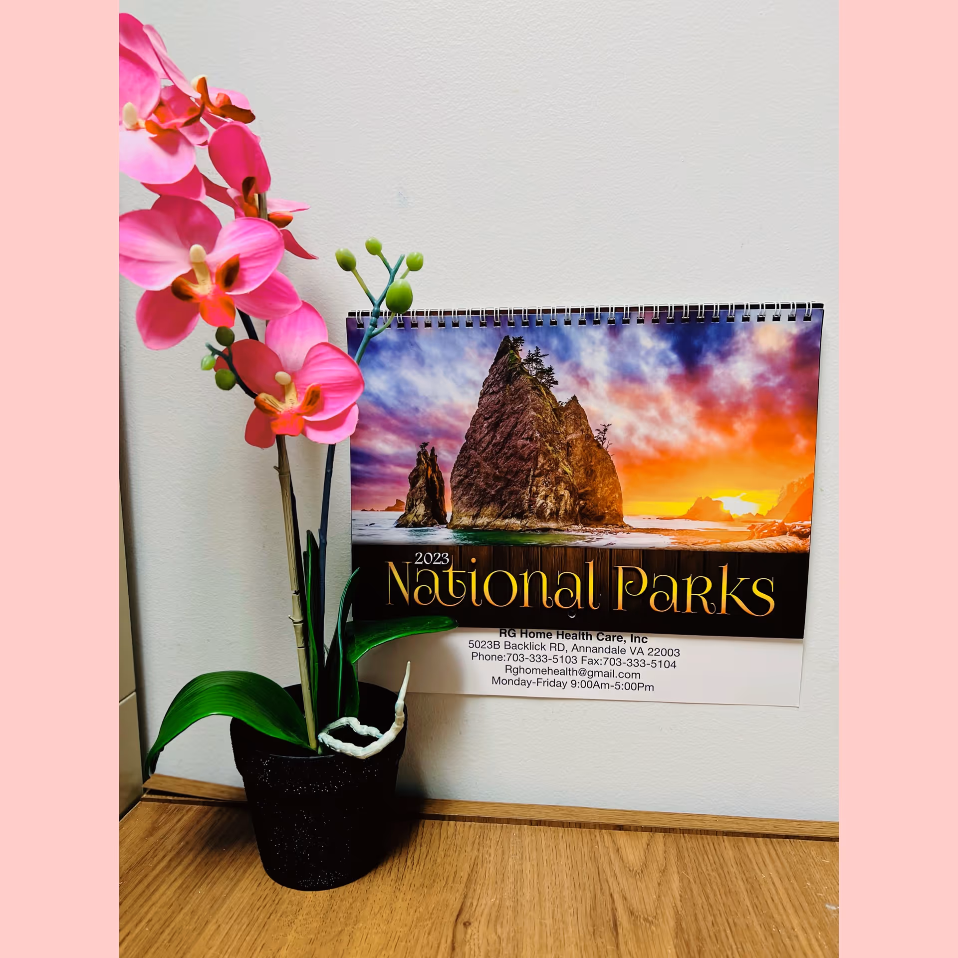 A potted pink orchid beside a National Parks calendar on a wooden desk.