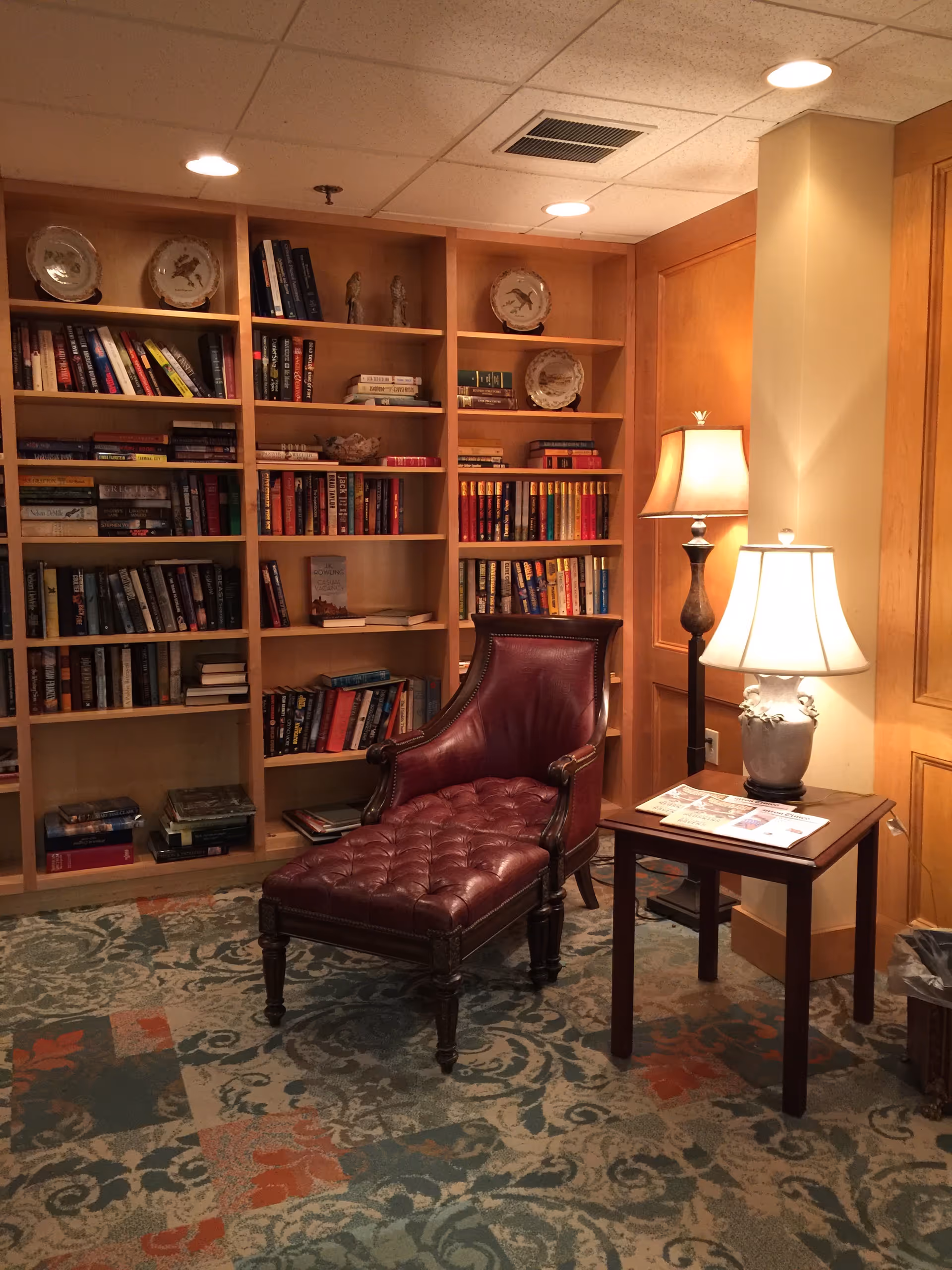 Cozy senior living lounge with a leather chaise, side table, and tall bookshelf.