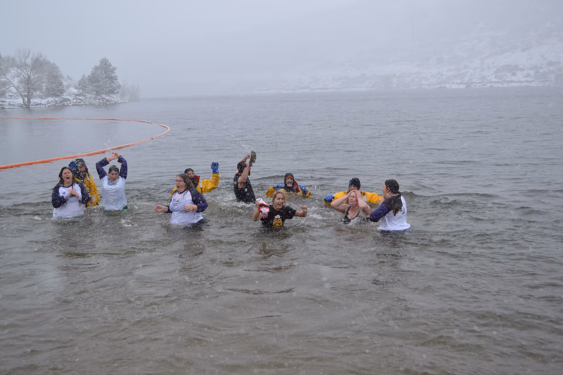 Group of people wading and splashing in a lake with snowy shores.