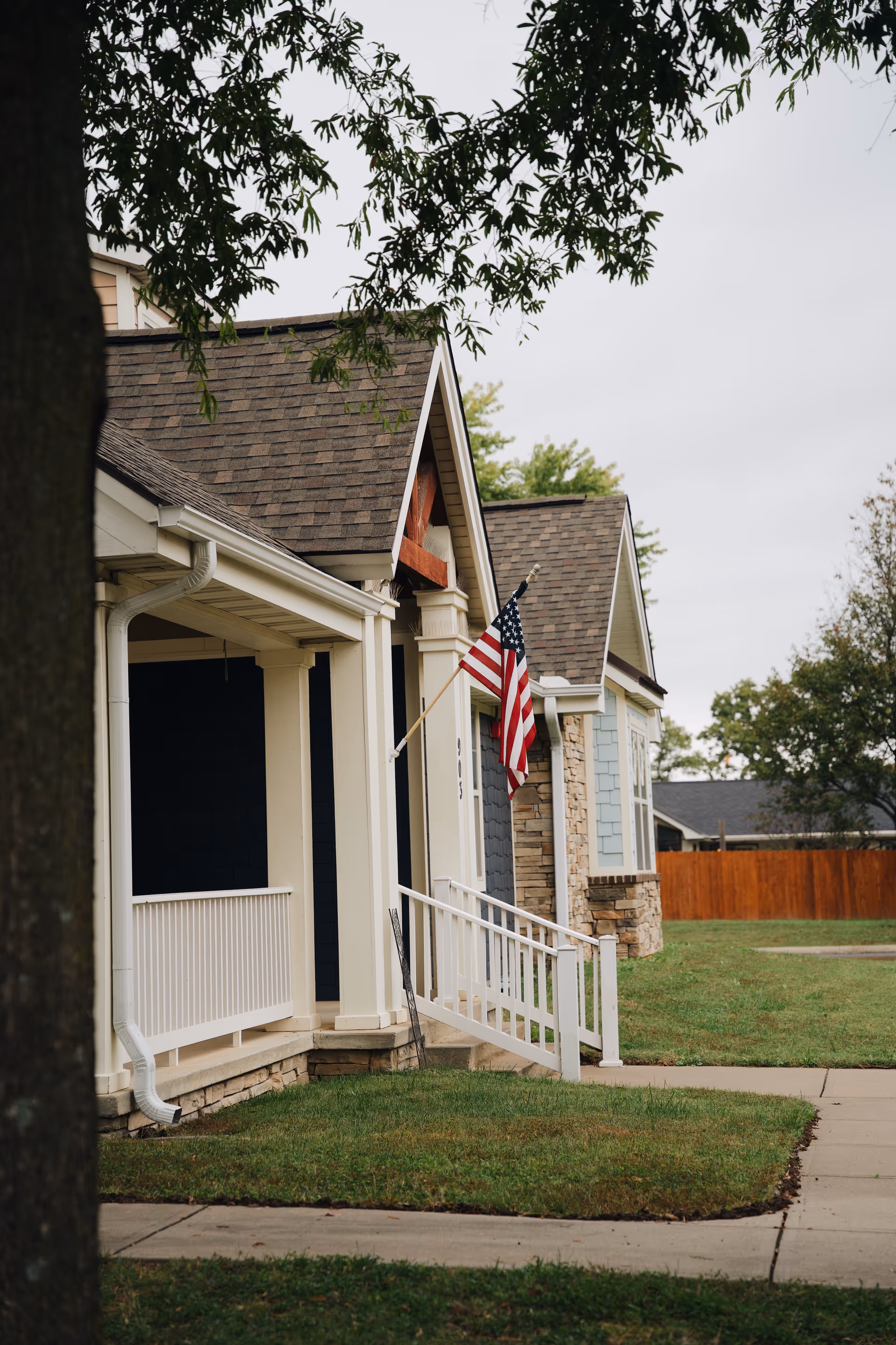 Front exterior of a senior living facility with a porch, flag, and neatly trimmed lawn.