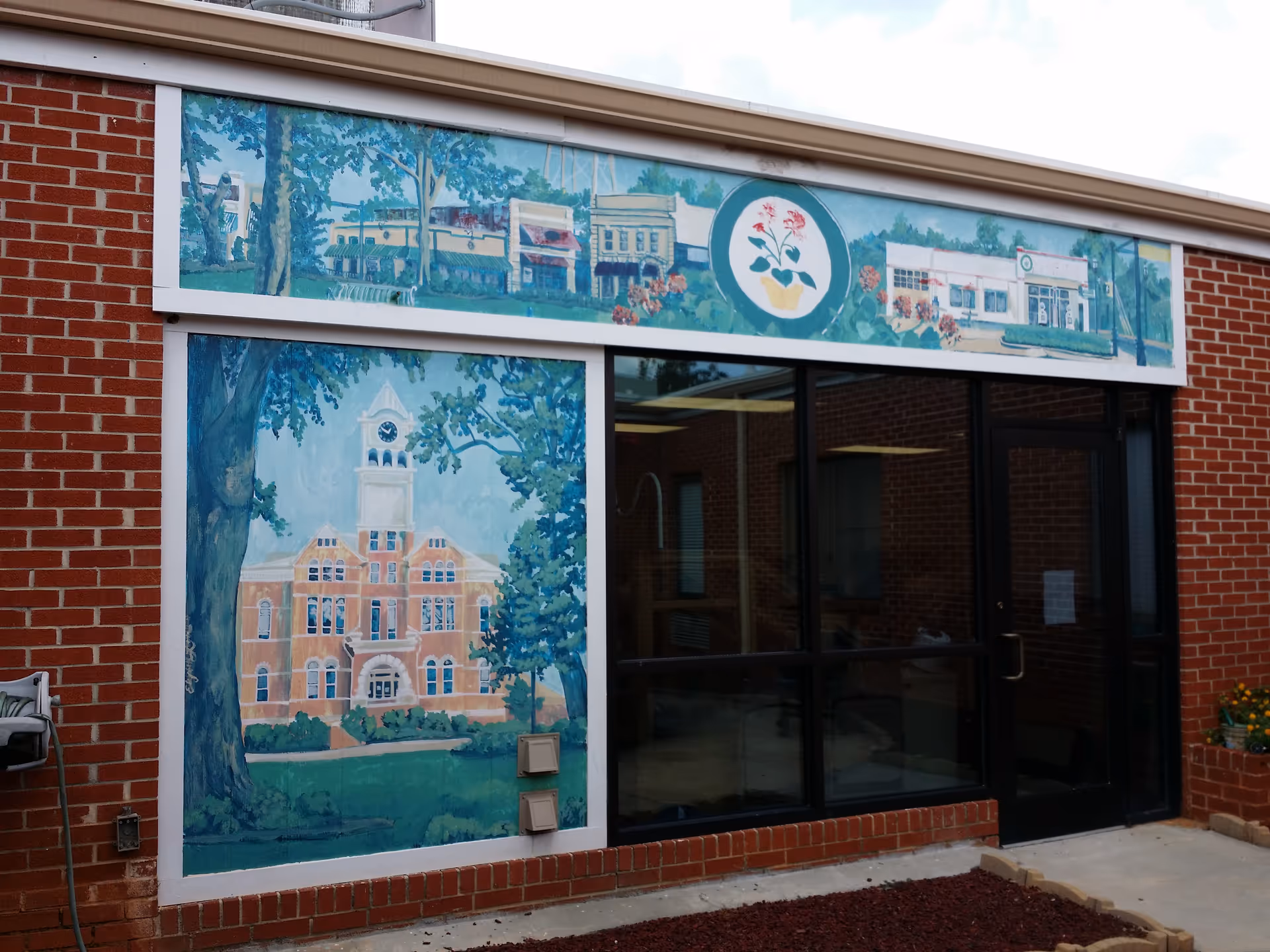 Brick building front with large mural panels depicting campus buildings and trees.