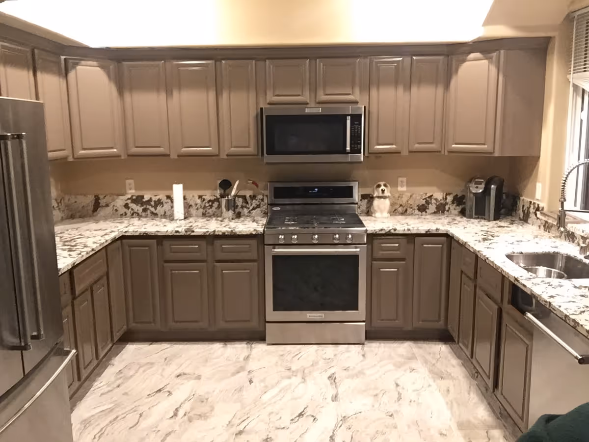 U-shaped kitchen with beige cabinets, marble countertops, stainless steel stove and refrigerator, and a sink under a window.