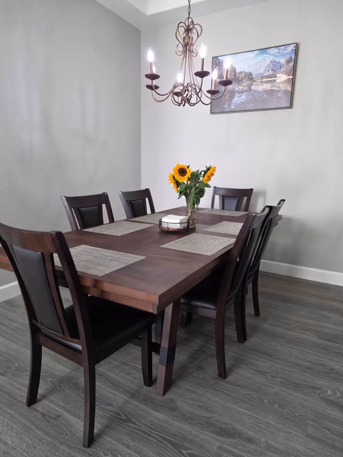 Dark wood dining table with six chairs and sunflowers in a bright dining room.