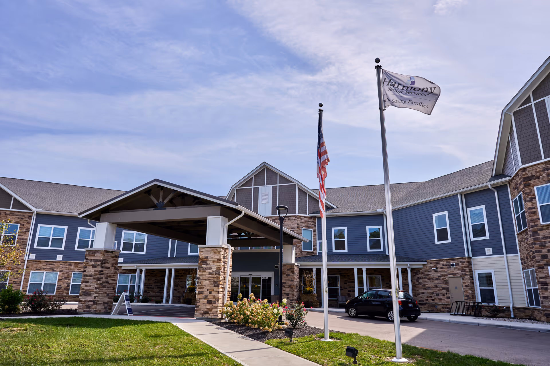Front view of Harmony at Anderson senior living facility with entrance canopy and flagpoles.
