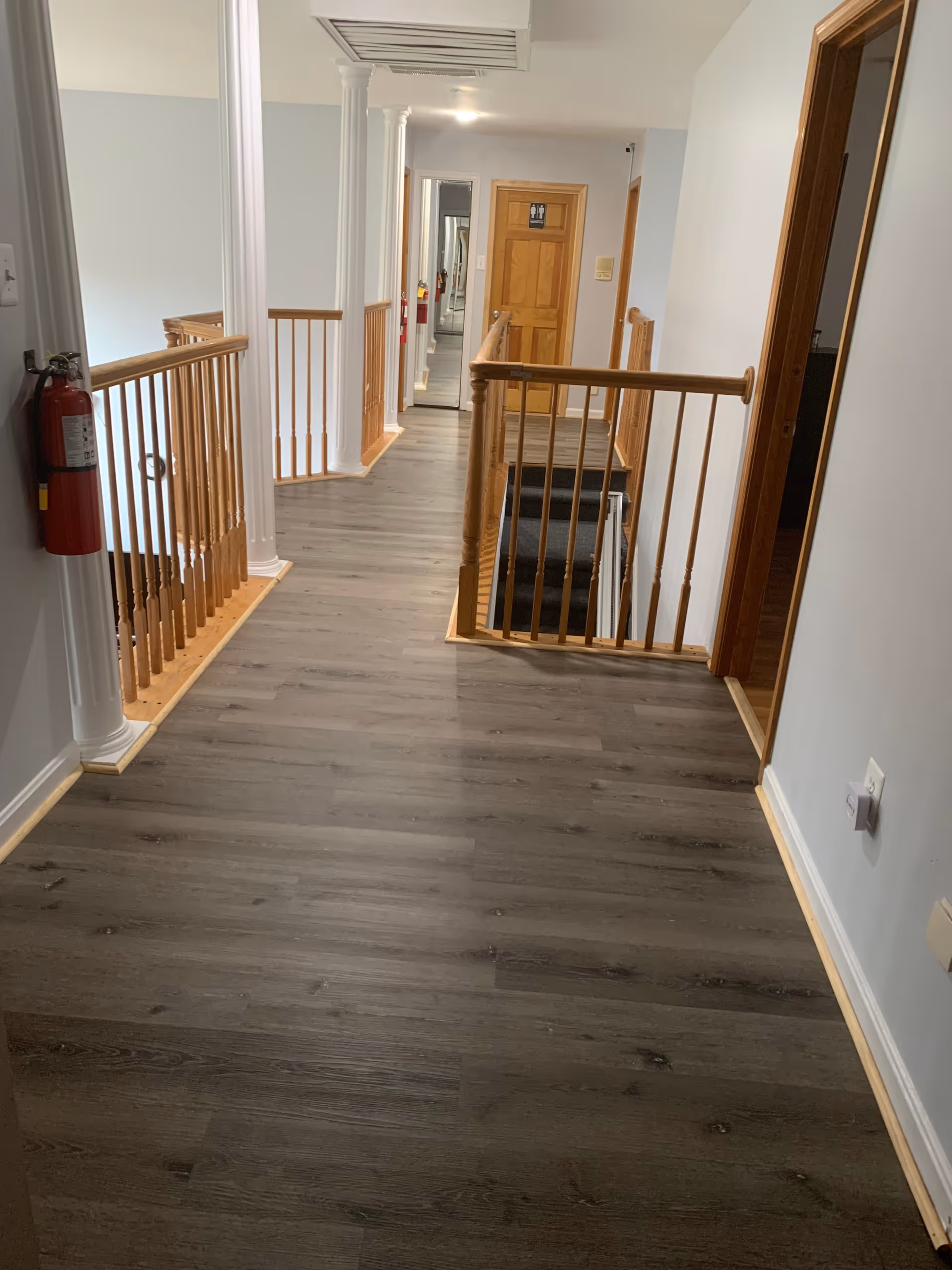 Upstairs interior hallway with wood railings, white columns, dark laminate flooring and a staircase.