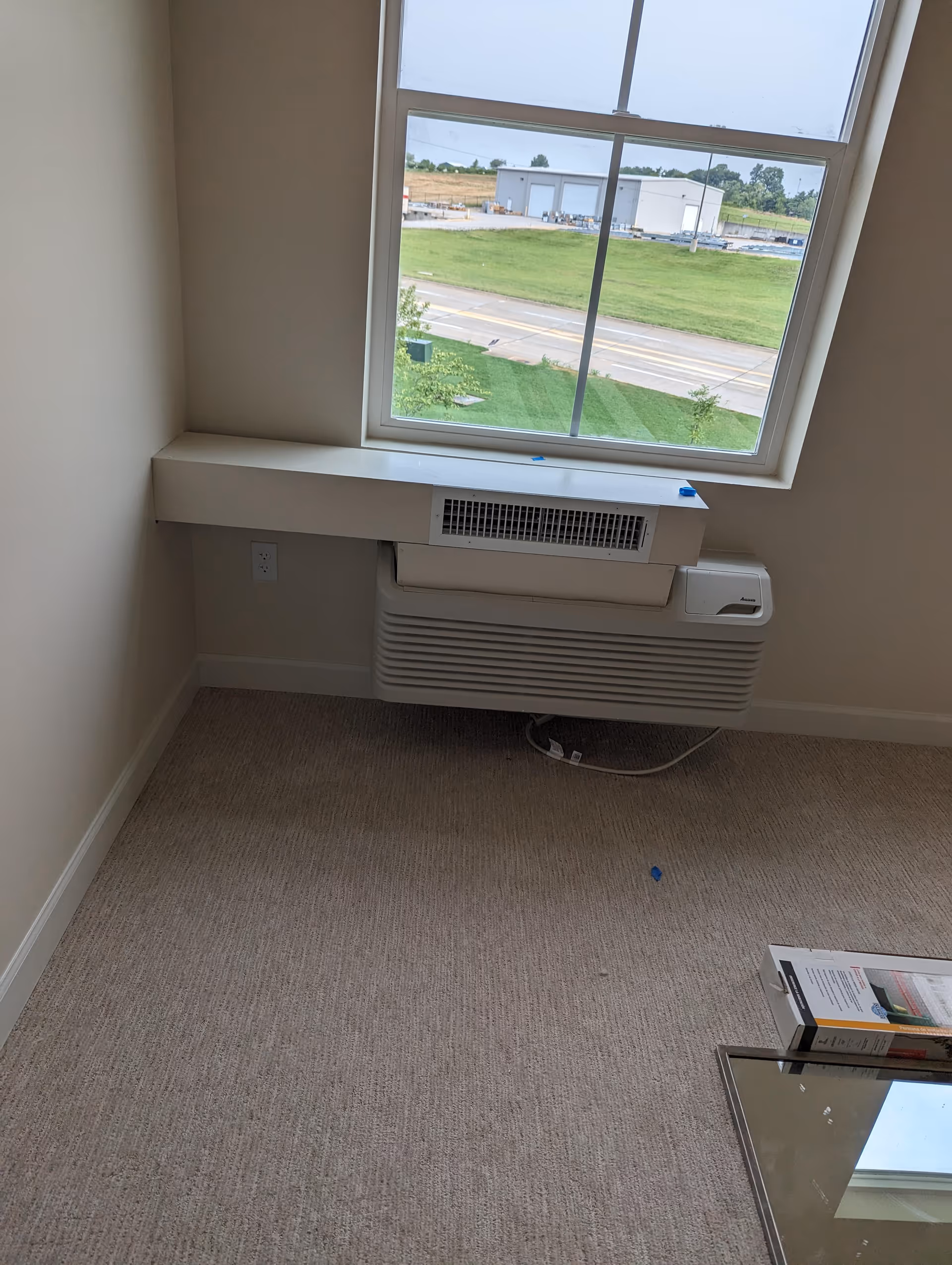 Empty beige room corner with a large window and wall heater.