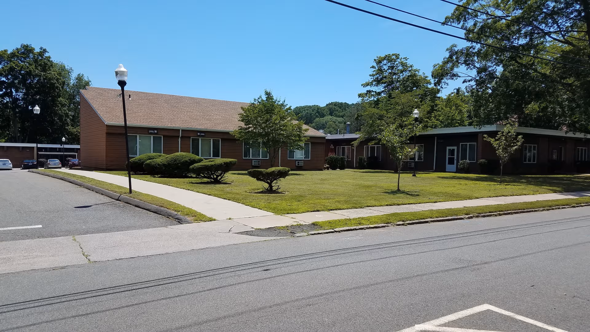 Single-story brick building with a well-kept lawn, trees, and a sidewalk.