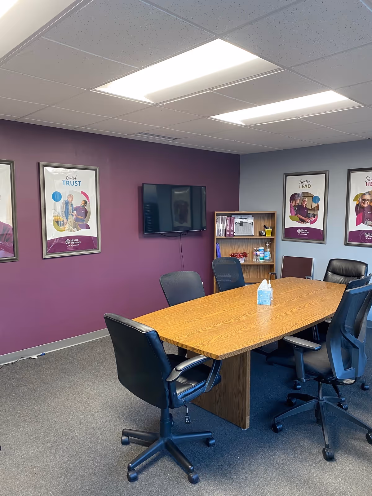 Conference room with a long wooden table, office chairs, and a wall-mounted TV.