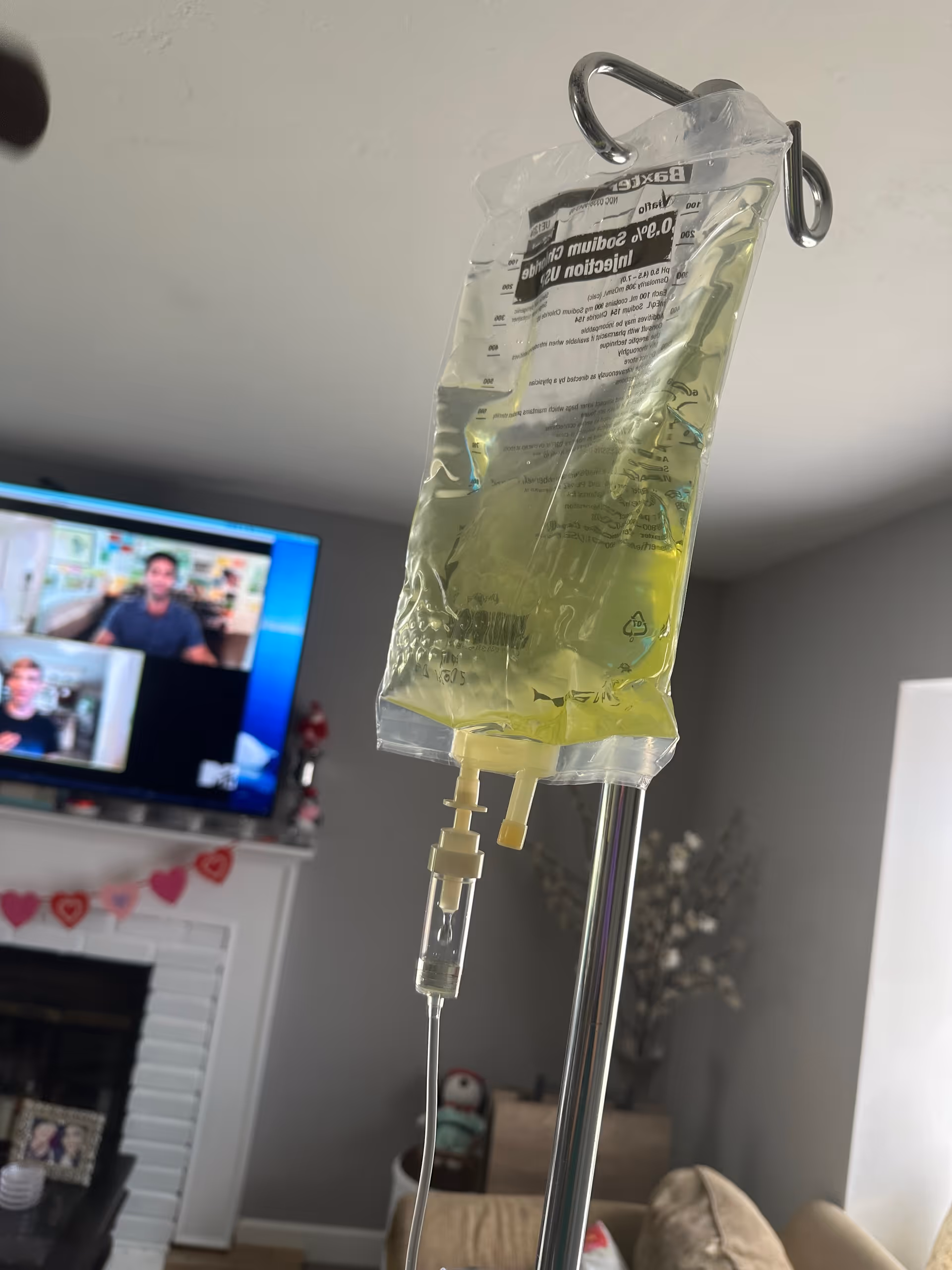 IV therapy bag on a stand in a living room beside a TV.