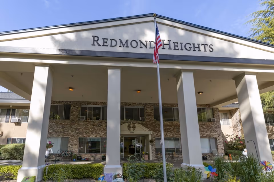 Front exterior view of Redmond Heights Senior Living building with columns and flag