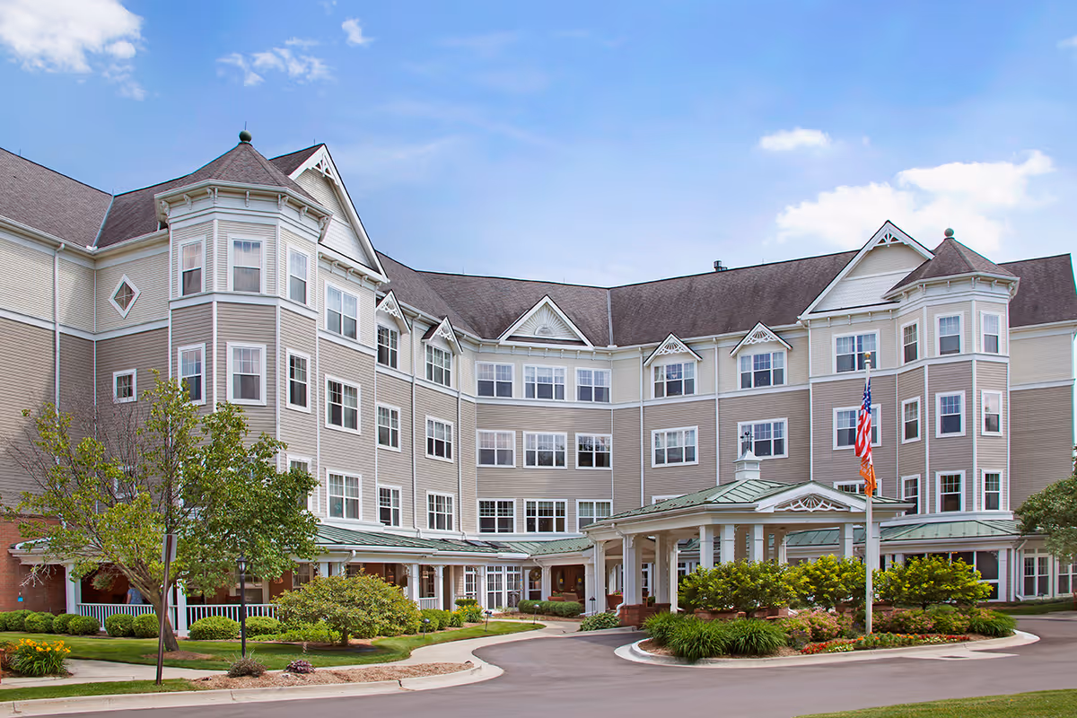 Beige, multi-story assisted living building with a covered entrance, circular driveway, and landscaped grounds.