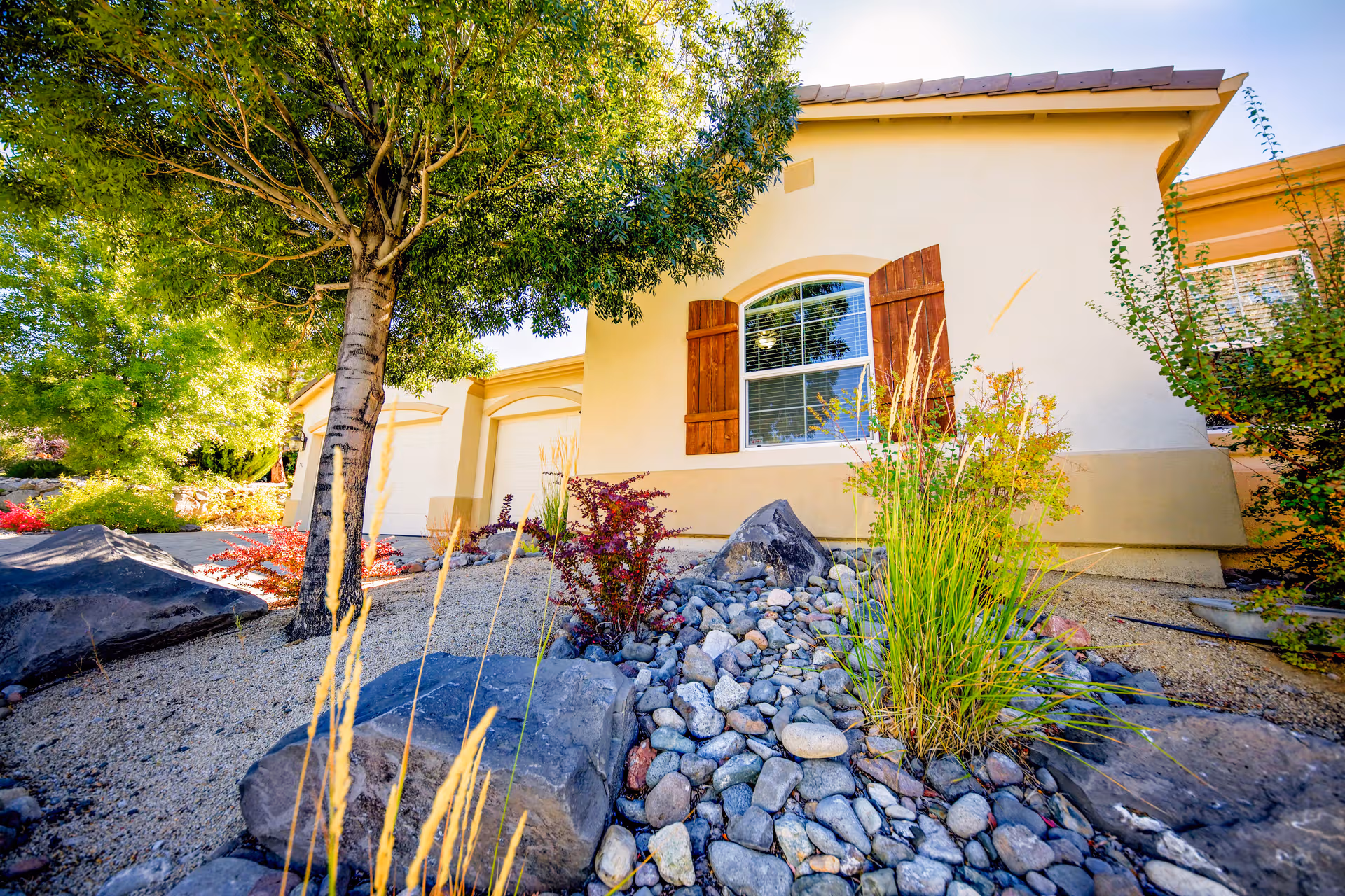 Front exterior of a single-story senior living facility with a landscaped rock garden and a tree.