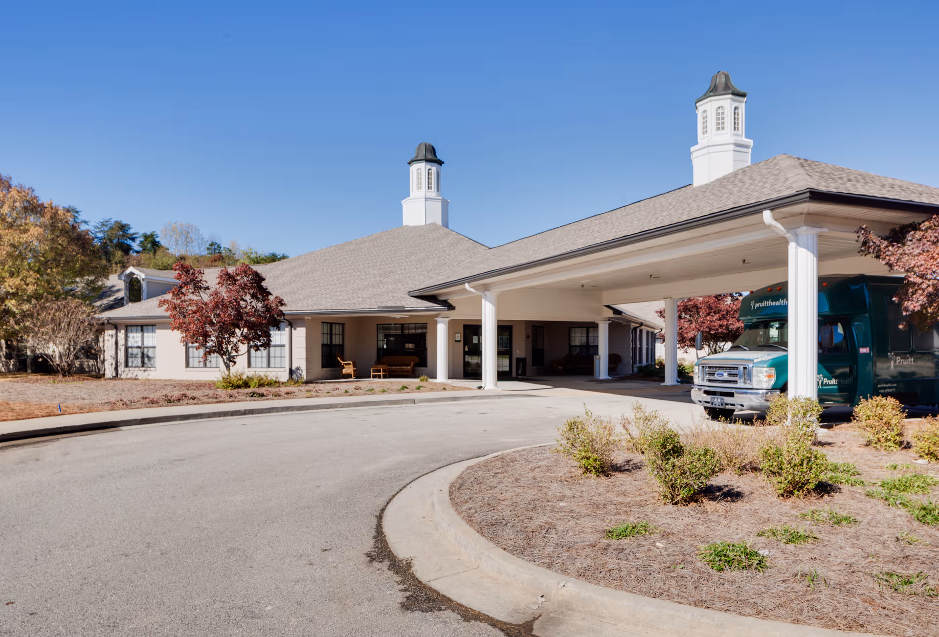 Exterior view of The Oaks Limestone facility showing driveway, porte-cochere entrance, and a parked bus.
