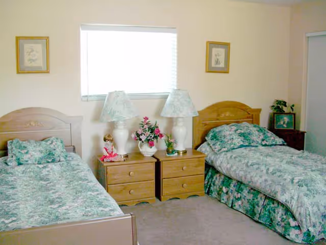 Twin beds with green floral bedding flank wooden nightstands and lamps.