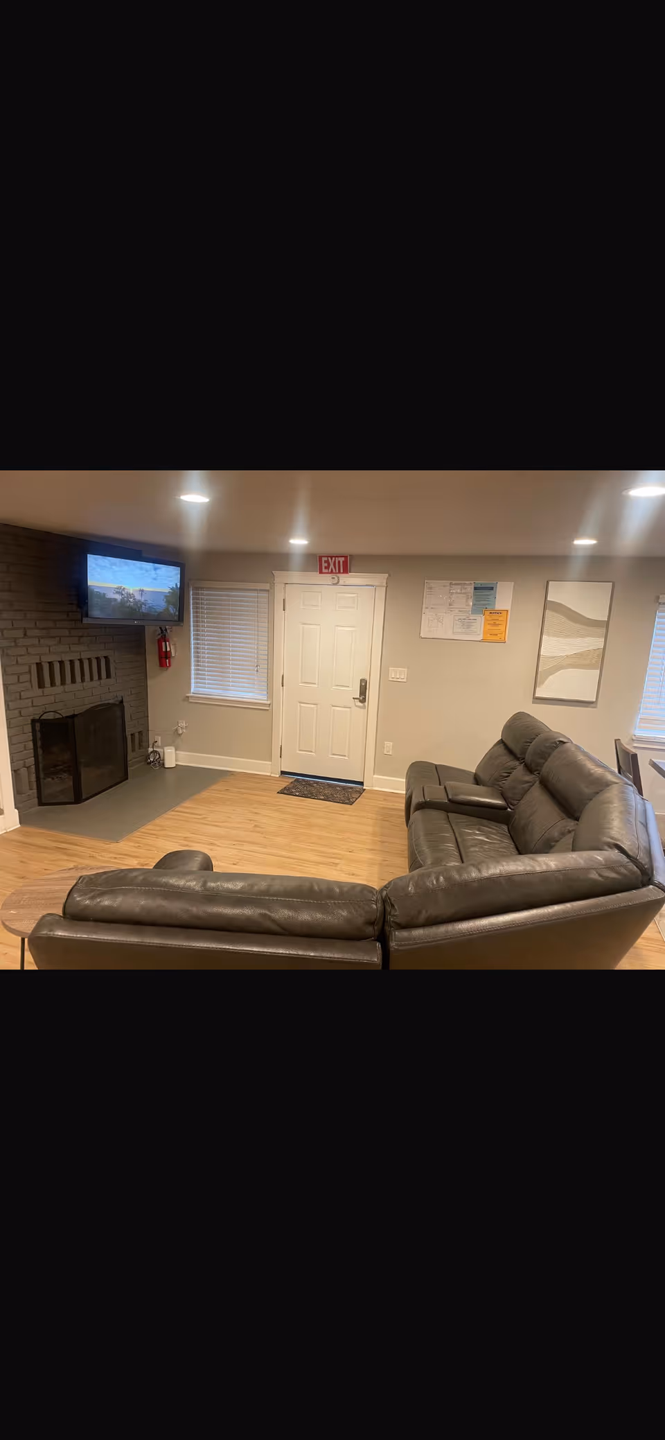 Cozy living room with leather sofas, a fireplace, TV, and an exit door.