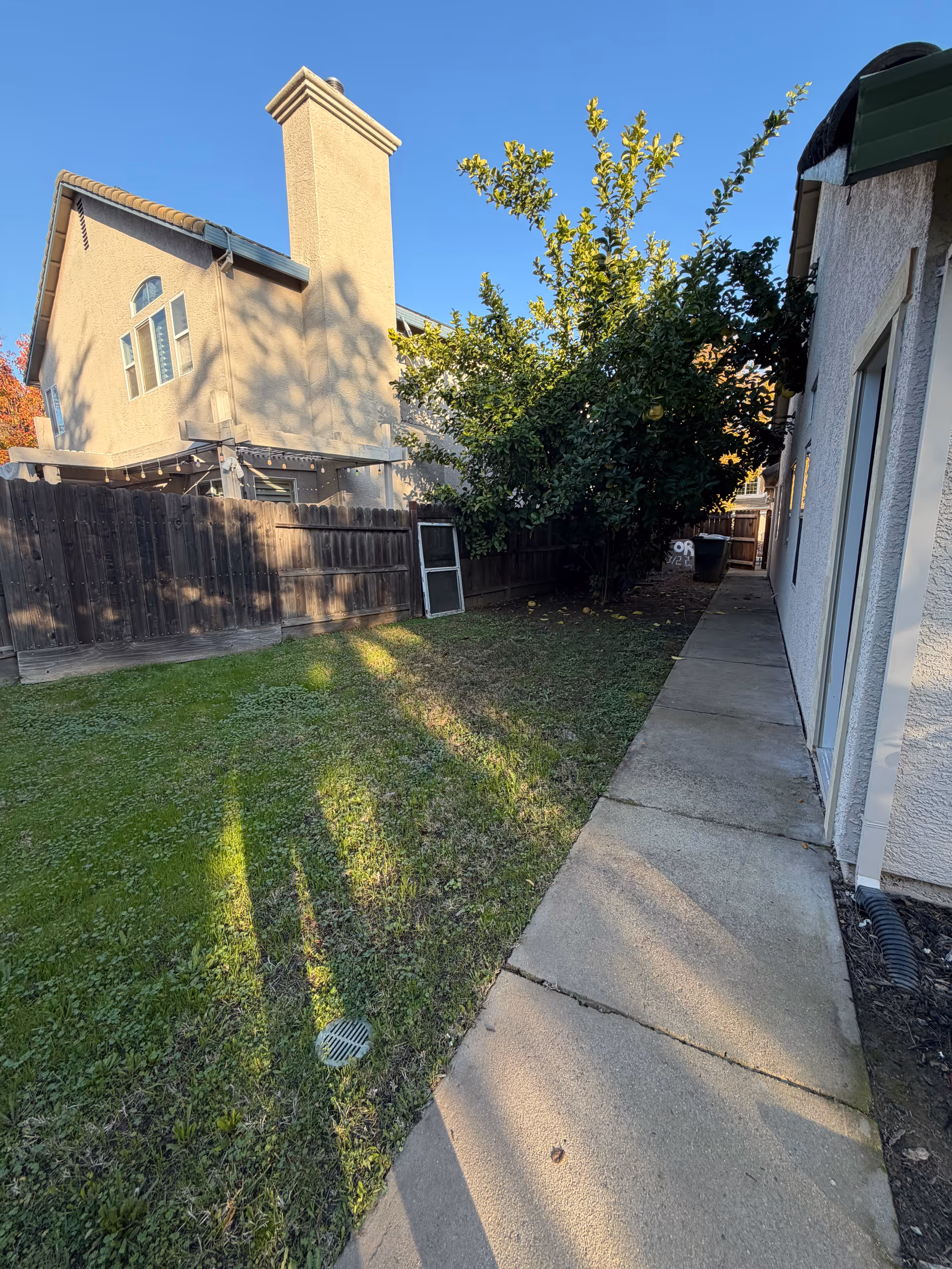 Outdoor backyard of a senior living facility with a concrete walkway, fence, and trees.