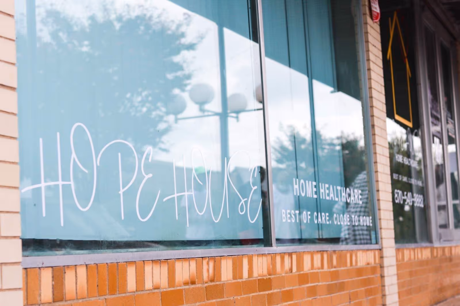 Exterior of a Hope House Home Healthcare storefront with teal windows and brick wall.