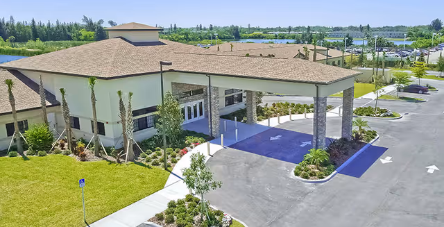 Exterior view of a senior living facility entrance with a porte-cochere and parking.