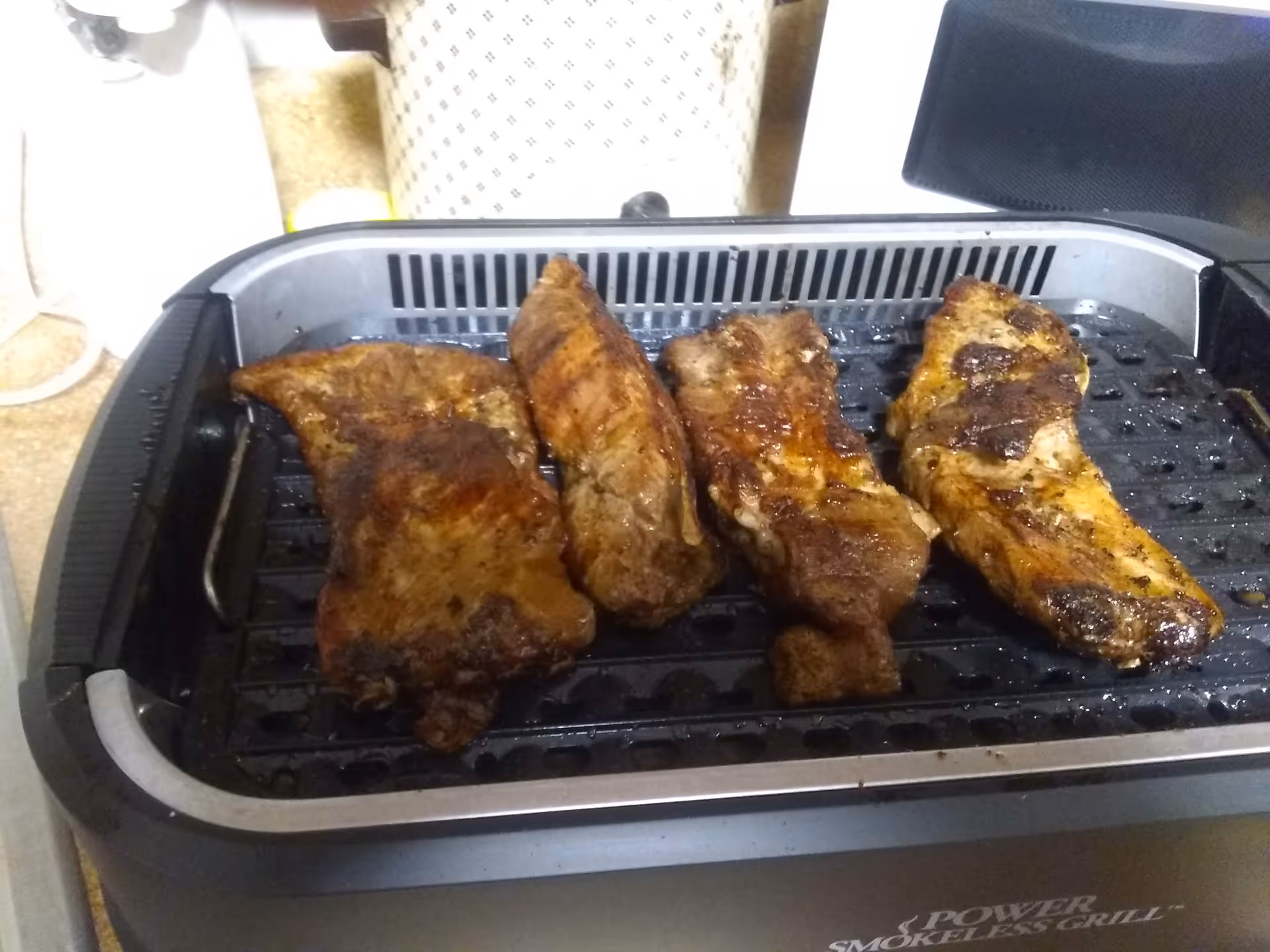Several cooked pork ribs on a countertop electric grill.