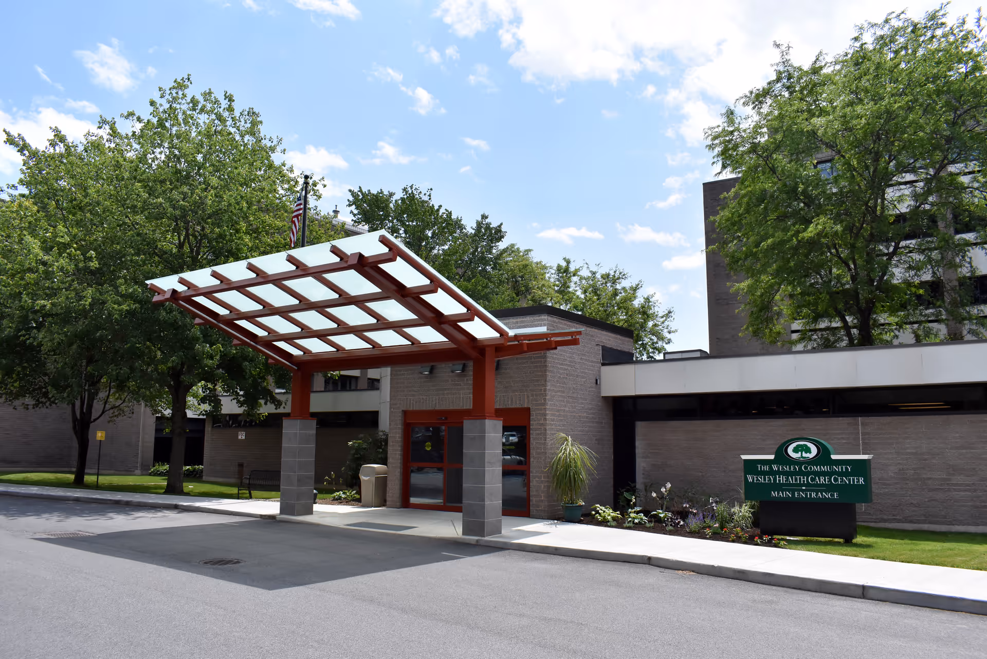 Exterior view of The Wesley Community entrance with a red canopy and a main entrance sign.