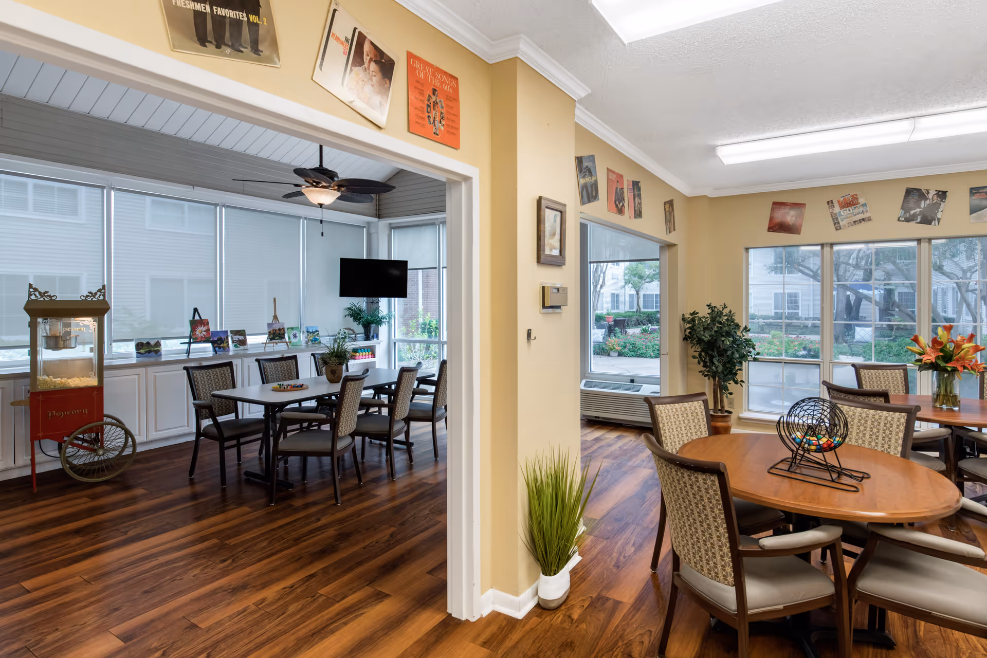 Indoor dining area at a senior living facility with round tables, chairs, decor, and large windows.