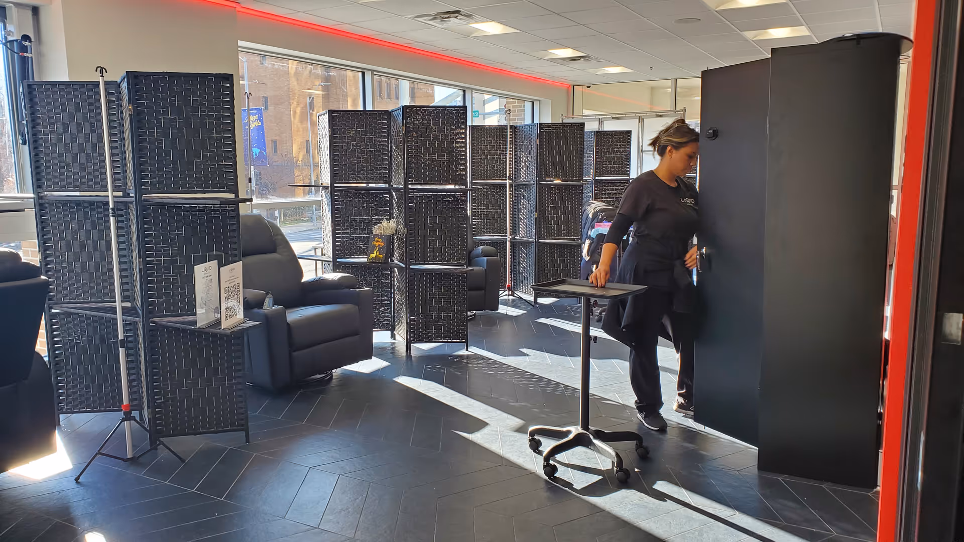 A staff member stands near a tall dark cabinet in a modern, partitioned waiting area.