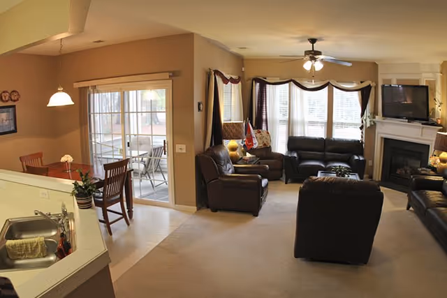 Cozy living room in a senior facility with leather sofas, fireplace, and large windows.