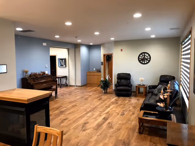 Interior common area with leather recliners, piano, plants, and wood flooring.