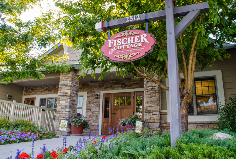 Exterior view of Fischer Cottage entrance at St. John’s United, with stone façade and flowers.