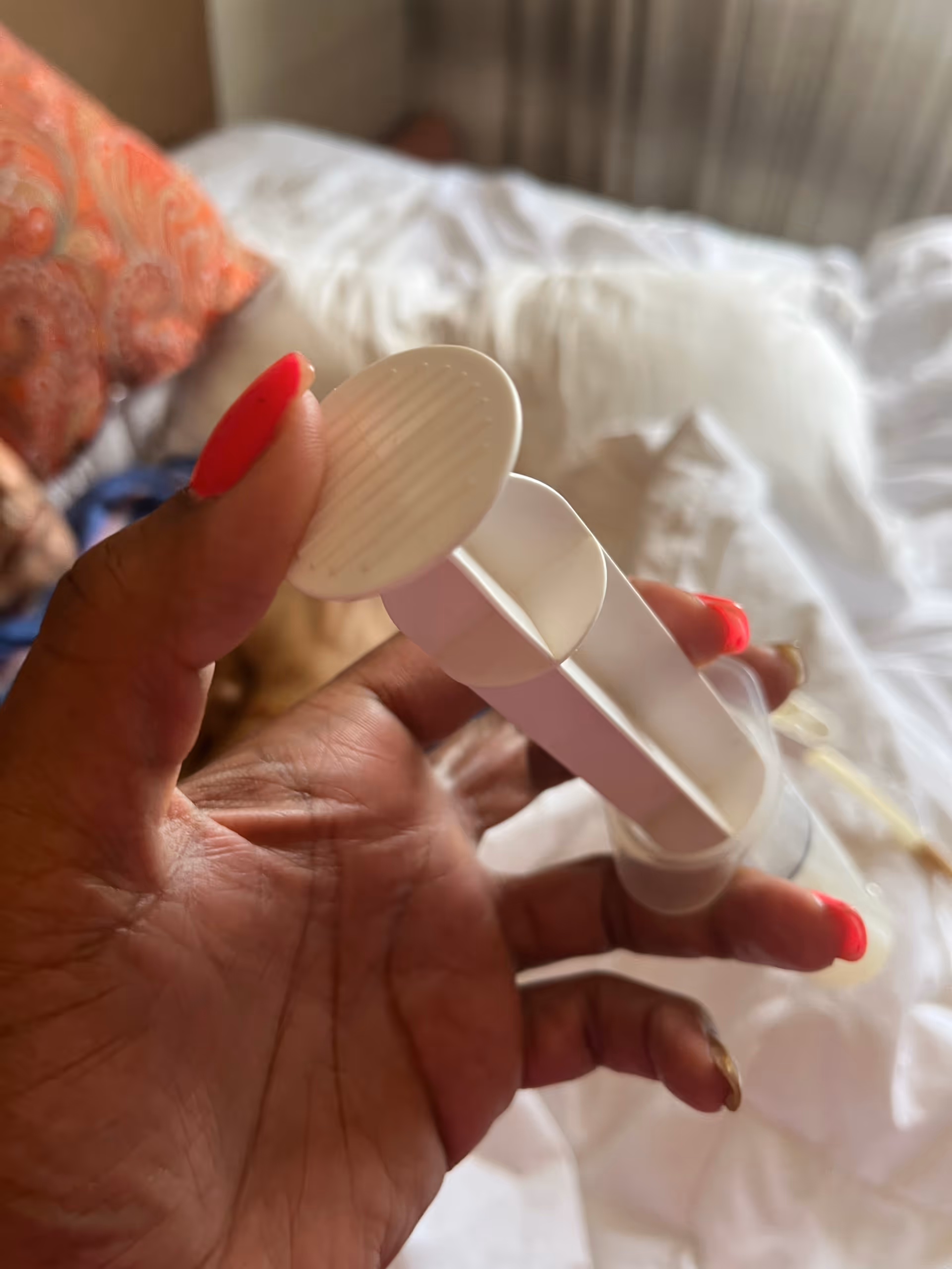 Close-up of a hand holding a white, multi-compartment pill organizer over a bed.