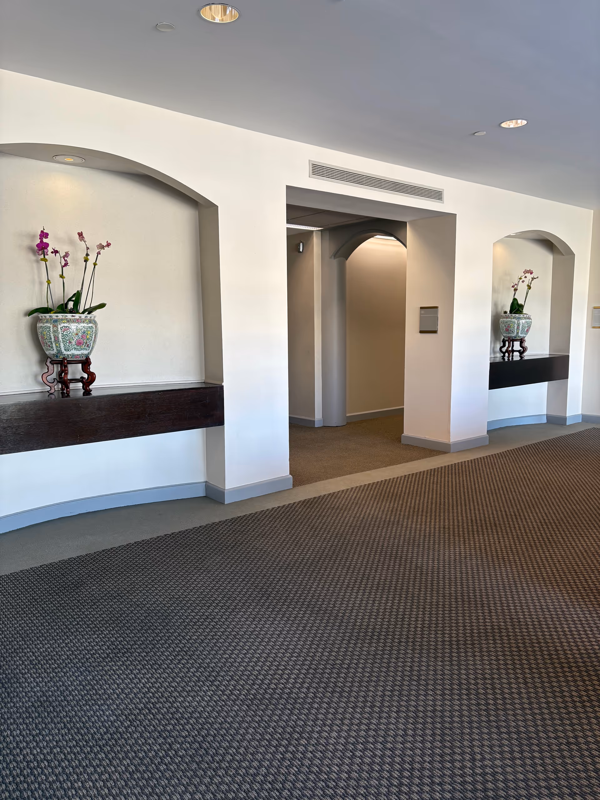 Interior hallway with arches and decorative orchid vases on shelves.