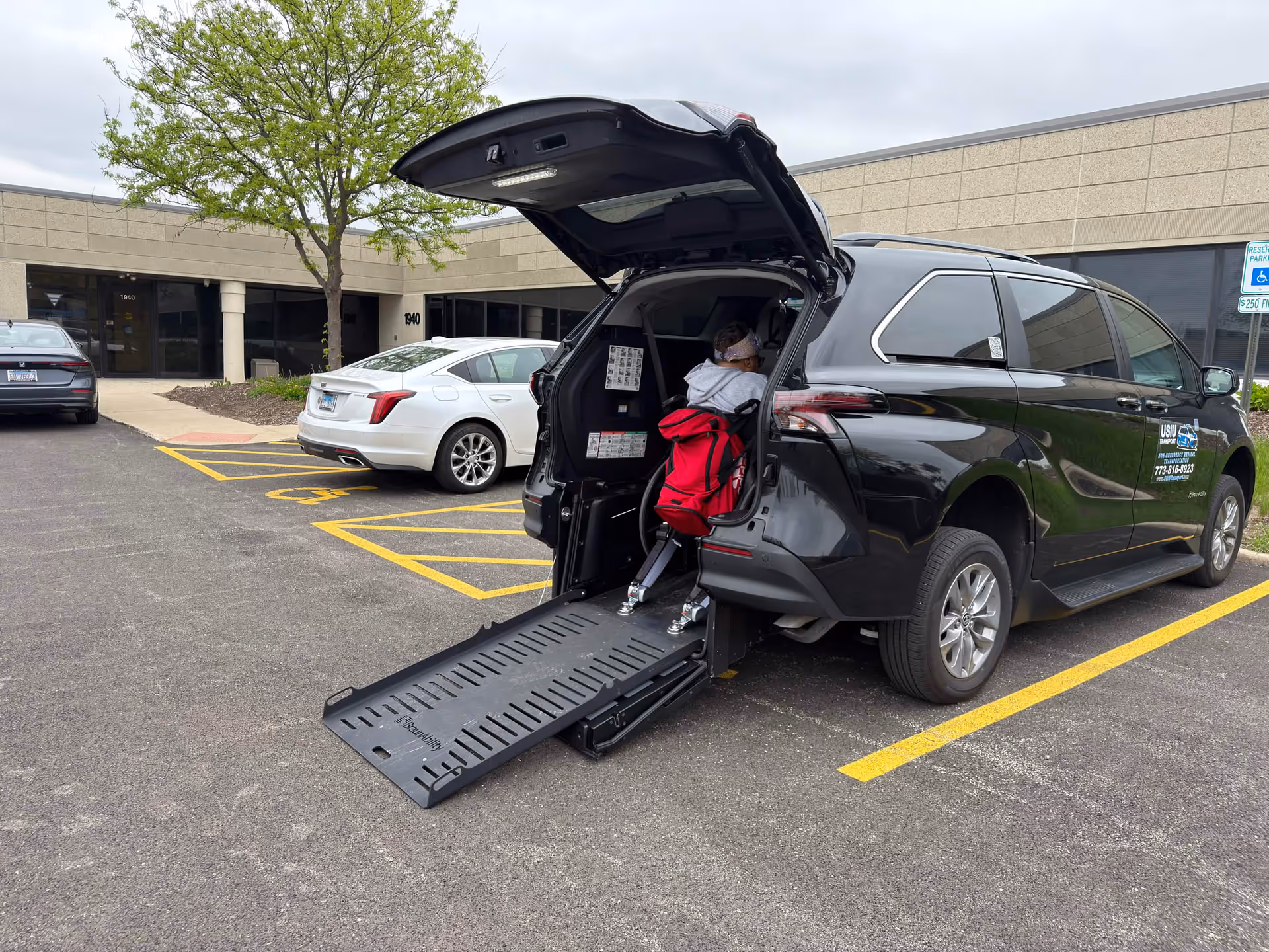 Person in wheelchair loading into a ramp-equipped van outside a building.